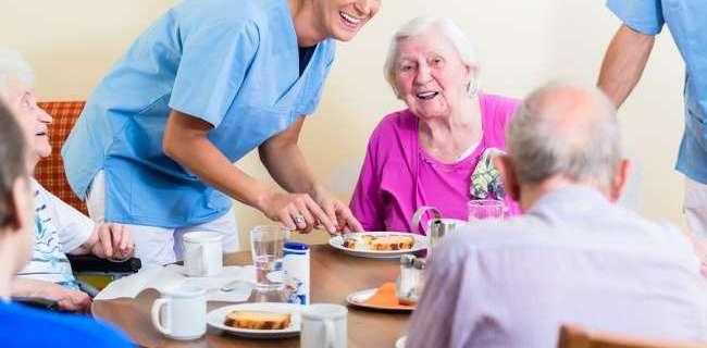 Group of seniors having food in nursing home, a nurse is serving